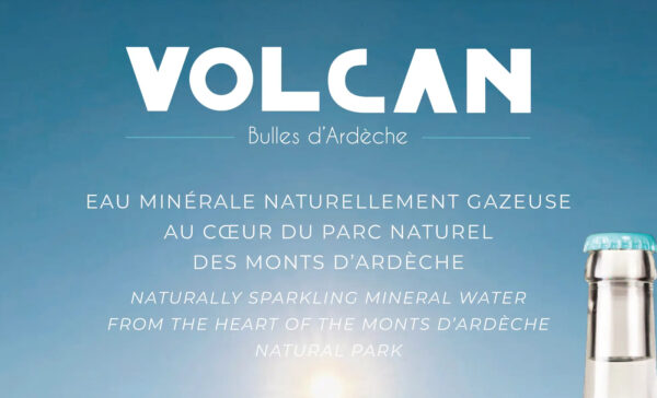 Image de couverture publicitaire pour la marque "Volcan - Bulles d'Ardèche". Le visuel présente un fond de ciel bleu azur dégradé avec un soleil lumineux en partie basse. Le texte est centré en lettres blanches, indiquant en français et en anglais : "EAU MINÉRALE NATURELLEMENT GAZEUSE AU CŒUR DU PARC NATUREL DES MONTS D’ARDÈCHE". Dans le coin inférieur droit, on aperçoit le goulot d'une bouteille en verre transparent surmontée d'une capsule bleu turquoise.