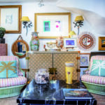 Ambiance feutrée et raffinée au sein de la boutique Mas Ermitage - Antiques & Design à Saint-Tropez. Composition intérieure mêlant des fauteuils en rotin aux coussins brodés de palmiers turquoise, une table en marbre noir veiné, un buffet graphique et une riche collection d'objets d'art, miroirs et tableaux anciens. Reportage exclusif réalisé pour l'édition de Juin 2026 de THE Magazine.