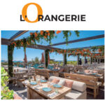 Reportage exclusif réalisé pour l'édition de Juin 2026 de THE Magazine au restaurant de plage L'Orangerie. Vue de la terrasse aménagée face à la mer avec sa pergola en bois fleurie de touches orange et ses tables dressées élégamment.