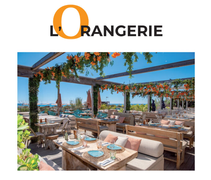 Reportage exclusif réalisé pour l'édition de Juin 2026 de THE Magazine au restaurant de plage L'Orangerie. Vue de la terrasse aménagée face à la mer avec sa pergola en bois fleurie de touches orange et ses tables dressées élégamment.