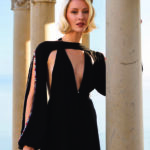 Cliché artistique plein format issu du shooting pour la maison de couture Ziya Shari à Saint-Tropez. Le mannequin pose avec élégance au cœur d'une structure de colonnes classiques éclairées par la lumière dorée du soleil couchant, face à la mer méditerranée. Visuel éditorial exclusif pour l'édition de Juin 2026 de THE Magazine.