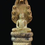 Photographie d'une antiquité d'exception issue de la collection Mas Ermitage à Saint-Tropez. Sculpture en pierre fine représentant Bouddha en méditation assis sur les anneaux du serpent Mucalinda, abrité par ses sept têtes déployées en aura protection. Cliché studio sur fond noir réalisé pour l'édition de Juin 2026 de THE Magazine.