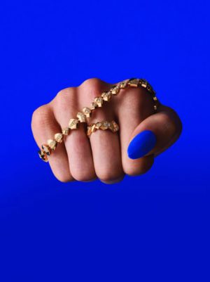 Visuel de campagne percutant pour la Maison Akillis Paris et sa collection emblématique Capture Me. Un poing fermé met en valeur un bracelet et une bague graphiques en or sertis de diamants, contrastant avec un vernis à ongles assorti au fond bleu électrique. Cliché exclusif intégré dans la section Joaillerie & Horlogerie de l'édition de Juin 2026 de THE Magazine.